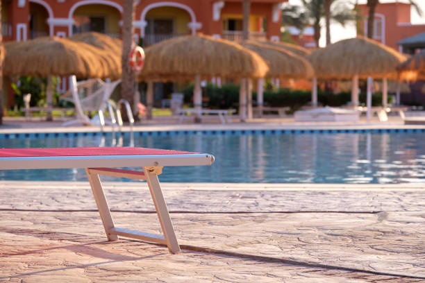 Empty deck chair on swimming pool side in summer resort. Vacations and getaway concept.