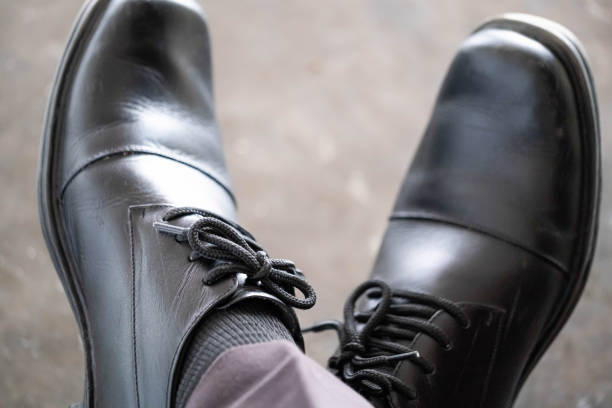 Close-up of a person wearing black leather dress shoes with laces, sitting with legs crossed.