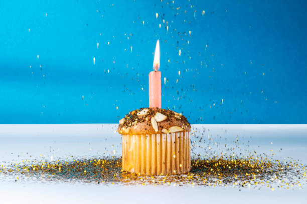 istock Birthday cupcake with single lit candle and golden glitter on blue background. Closeup 2159770148