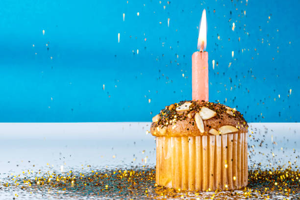 istock Birthday cupcake with single lit candle and golden glitter on blue background. Closeup 2159770175