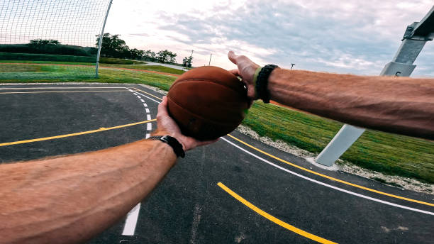 A player extends an arm to shoot a basketball in a competitive one-on-one outdoor game on a court with visible boundary lines and hoop.