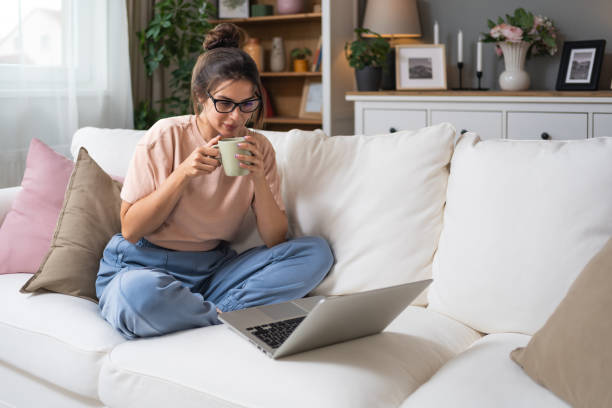istock Young woman online dating or telecommuting on video call from home while drinking coffee or tea with her boyfriend or friend on laptop computer. Female using technology in cozy apartment and relax. 2159787467
