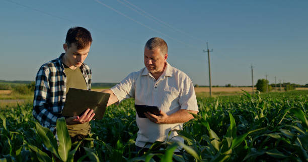 Two farmers working in a field, using a laptop and a tablet. Technology in agriculture
