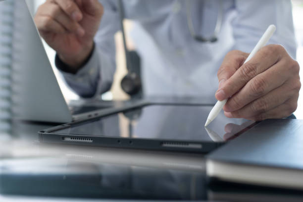 istock Doctor with stylus pen working on digital tablet and laptop computer at doctor's office, recording patient's illness. Electronic Health Record. Healthcare and medicine concept 2159790083