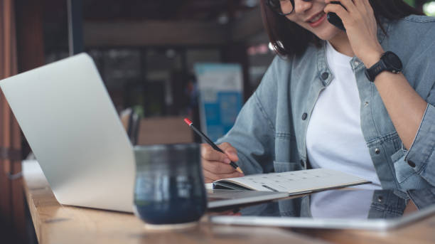 Smart asian business woman talking on mobile phone during planning work schedule with laptop computer and digital tablet on table at coffee shop. Happy businesswoman online working from cafe, business casual
