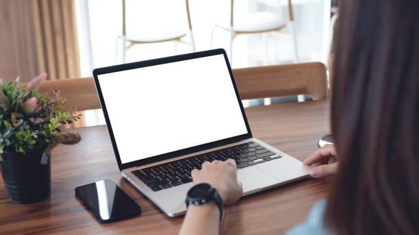 istock Mockup blank white screen laptop computer. Business woman using and searching the information on laptop with empty screen on wooden table in modern loft cafe. Back view, template for online marketing design 2159792748