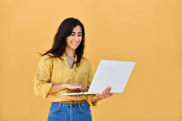 istock Focused young middle eastern brunette woman using laptop pc app for online business work, study isolated on yellow background. Arabian girl student in casual clothes holding computer, working remote 2159806260