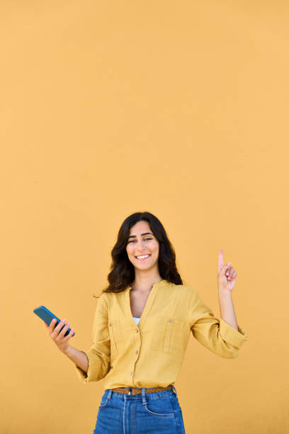 Young woman holding smartphone telephone, pointing up above at copy space for advertisement promo. Smiling brunette consumer girl, buyer using cellphone mobile phone for business. Isolated, vertical mujer joven sosteniendo un teléfono inteligente, apuntando hacia arriba en el espacio de copia para la promoción de la publicidad. chica consumidora morena sonriente, compradora que usa el teléfono móvil para el negocio. aislado, vertical