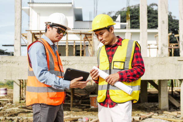 istock Two male construction workers, including an Asian engineer, meticulously review structural plans and design concrete columns and beams for a new residential build. 2159808506