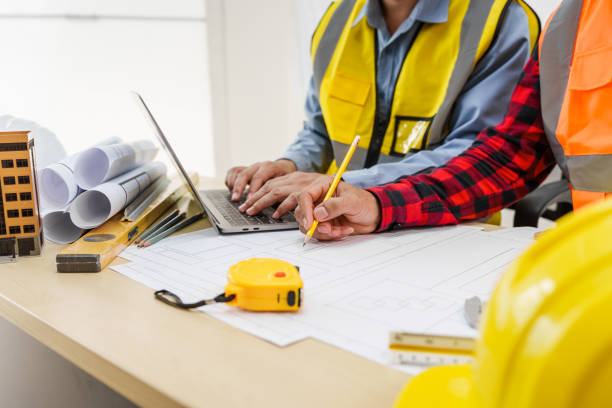 istock Two men, including a male Asian construction contractor engineer, discuss structural plans and engineering concrete columns and beams of a new house at a desk with a building tower model. 2159808529