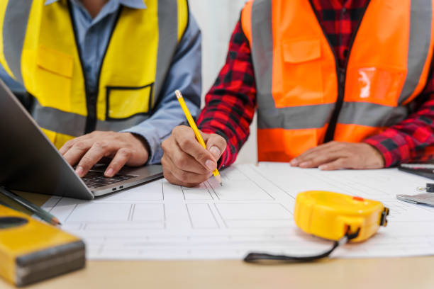 istock Two men, including a male Asian construction contractor engineer, discuss structural plans and engineering concrete columns and beams of a new house at a desk with a building tower model. 2159808535
