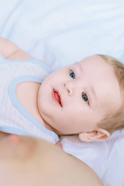 Close up portrait of a happy baby boy with bright blue eyes, lying on his back and smiling. He is wearing a blue and white onesie