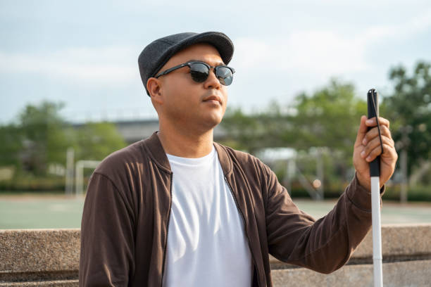 istock Young asian blind man sitting outside holding walking stick Visually impaired man difficult to traveling on the road wearing sun glasses Cross the road cross the footbridge 2159812369