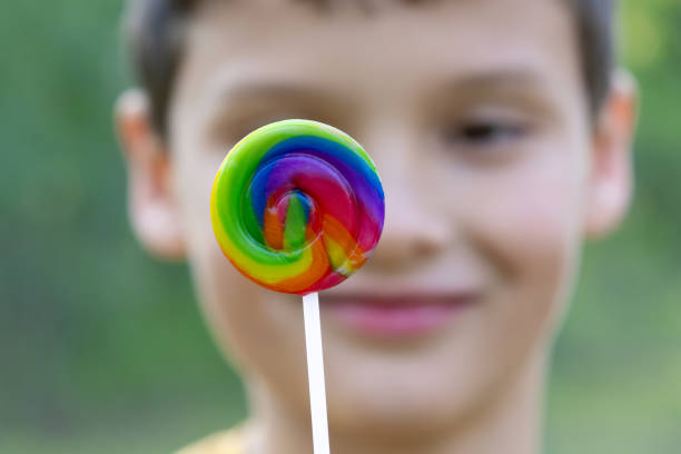 Close-up of colorful round spiral lollipop and a face of a smiling boy on the background.