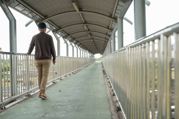 istock Young blind man walking in city with walking stick. Visually impaired man difficult to traveling on the road wearing sun glasses Cross the road cross the footbridge 2159813389