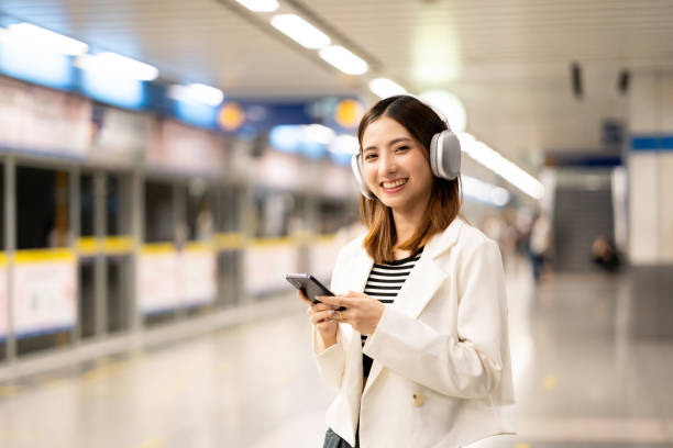 istock Young asian woman using smartphone application navigate location destination while travel by subway. Asian female with headphone listen to the music by cell phone while traveling in train transport 2159814913