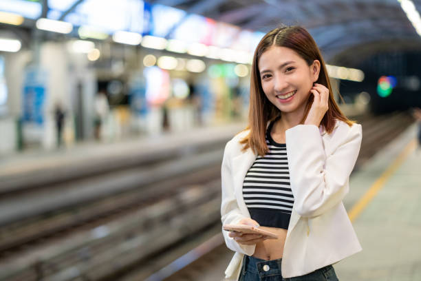 istock Young asian woman using smartphone application navigate location destination while travel by train. Asian female with cell phone standing near railway platform in train station. 2159814942