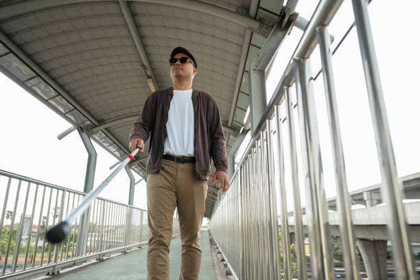 istock Young blind man walking in city with walking stick. Visually impaired man difficult to traveling on the road wearing sun glasses Cross the road cross the footbridge 2159814968