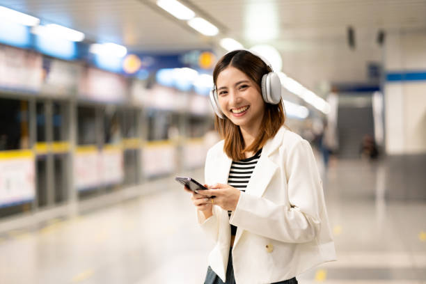 istock Young asian woman using smartphone application navigate location destination while travel by subway. Asian female with headphone listen to the music by cell phone while traveling in train transport 2159815197