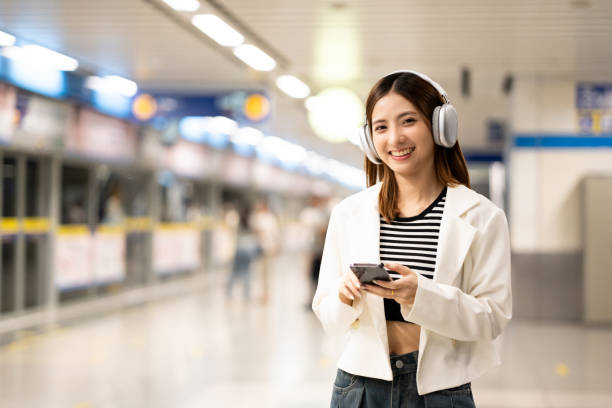 istock Young asian woman using smartphone application navigate location destination while travel by subway. Asian female with headphone listen to the music by cell phone while traveling in train transport 2159815524