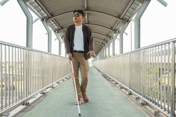 istock Young blind man walking in city with walking stick. Visually impaired man difficult to traveling on the road wearing sun glasses Cross the road cross the footbridge 2159815559