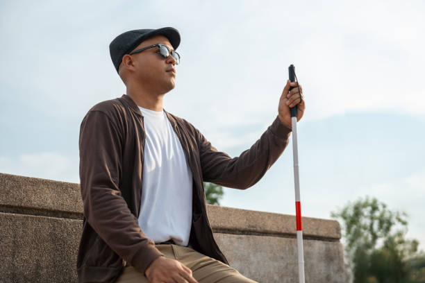 istock Young asian blind man sitting outside holding walking stick Visually impaired man difficult to traveling on the road wearing sun glasses Cross the road cross the footbridge 2159815787