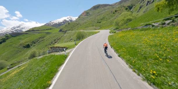 Road biker rides up high mountain pass, Gotthard Pass