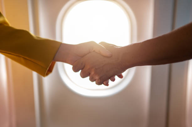 Pilot and stewardess shaking hands on airfield background.