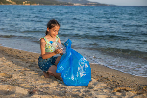 Young girls pick up trash on the local beach. Empty used dirty plastic bottles.
