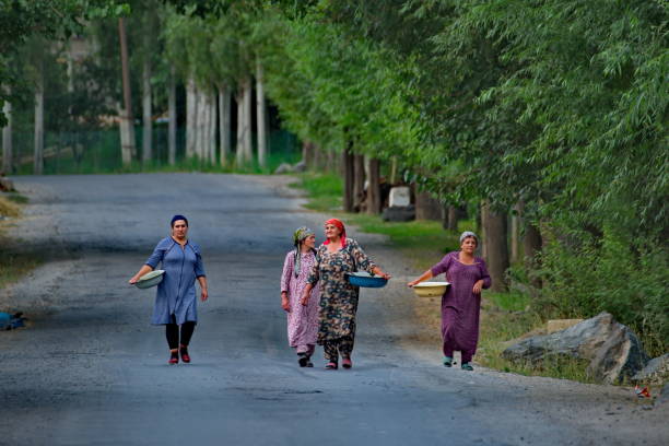 Darshai, Tajikistan. August 08, 2019. A group of village women with laundry basins in their hands walk along the asphalt of the Pamir highway along the bank of the border Panj River.