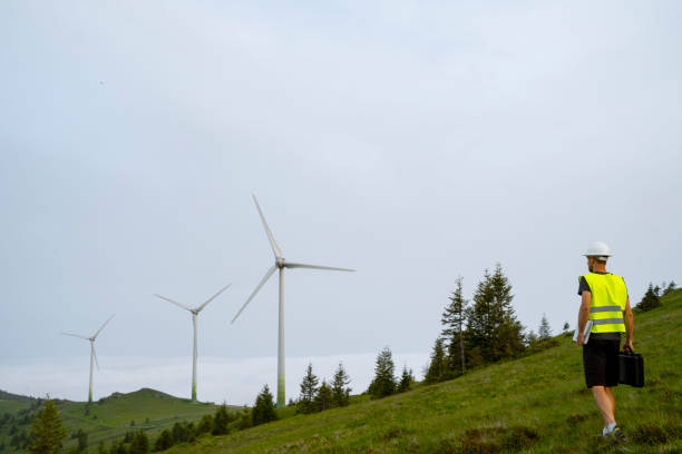 The worker is holding a clipboard and appears to be inspecting the turbines.
