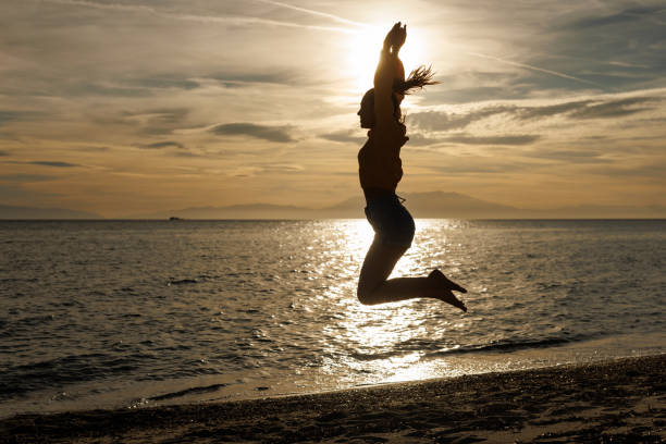 istock Happy young woman jumping on the beach at sunset 2159830109