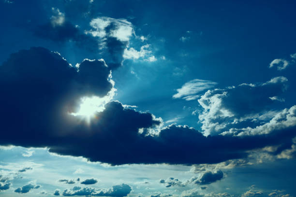 Sky is cloudy and the sun is shining through the clouds. Bright sun rays piercing through fluffy clouds