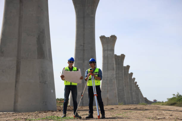 istock Two male  construction engineers  in safety vests and helmets discussing plans under the motorway  bridge at the construction site 2159842921