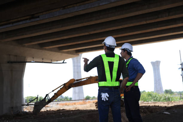 istock Two male  construction engineers  in safety vests and helmets discussing plans under the motorway  bridge at the construction site 2159842971
