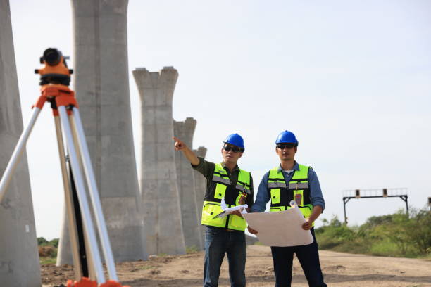 istock Survey construction technicians wearing safety vests and hard hats work with level survey cameras at road construction  site 2159842974