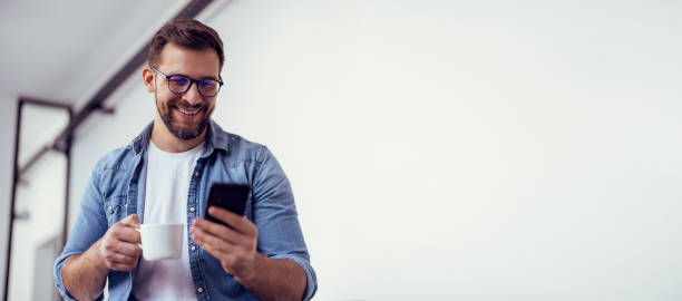 Handsome bearded man leaning on office desk, drinking coffee and talking on the phone.