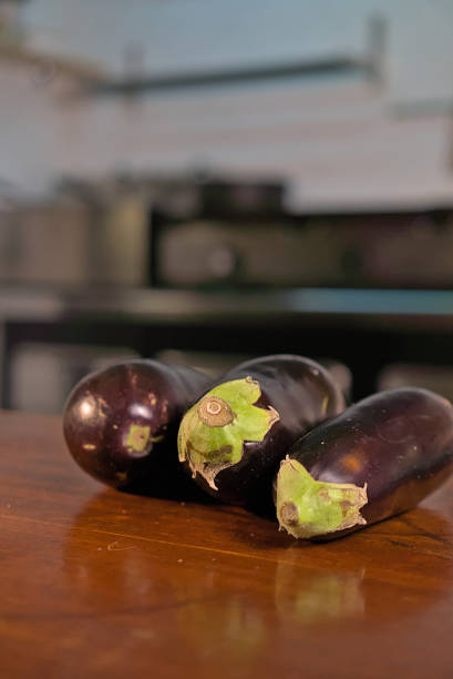 Fresh eggplants resting on a wooden kitchen counter, highlighting their vibrant purple hue and smooth texture, perfect for culinary themes and vegetable-focused content.
