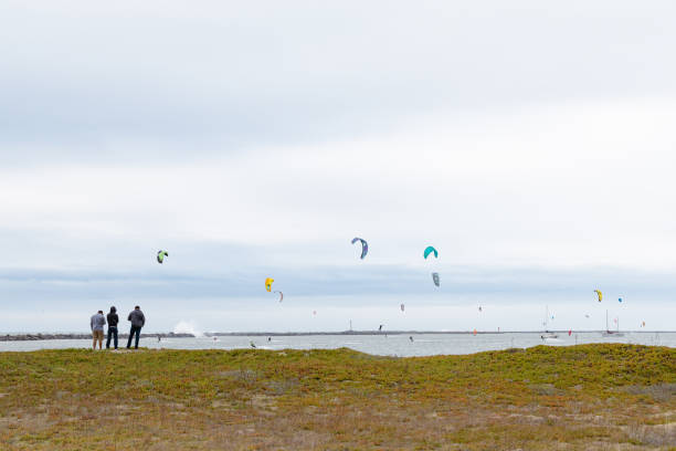 Half Moon Bay, California. December 23, 2023. Kiteboarders out on the water while pedestrians gather to watch from the beach.