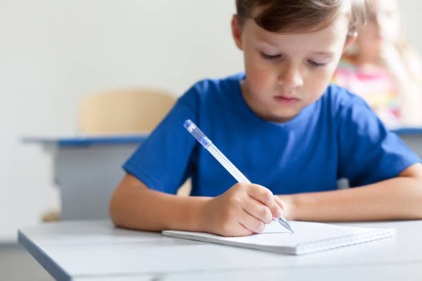 istock School child writing test on lesson. Pupil sitting at desk in classroom. Kid studying in elementary college. Primary student back to school. Education for children. Boy wearing in blue casual t-shirt 2159868090