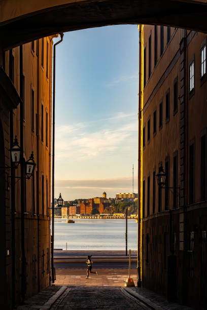Stockholm, Sweden June 24, 2024 A jogger passes  by a narrow alley on Norra Bankogrand on Old Town or Gamla Stan.