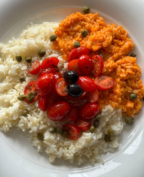 istock Rice dish with half plain white rice with capers, olives and cherry tomatoes and half with risotto and tomato sauce 2159877078