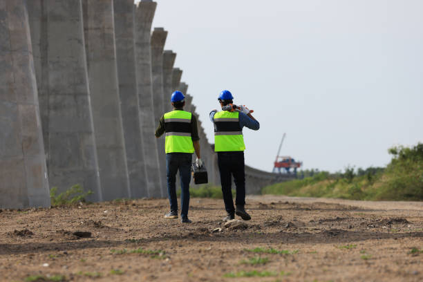 istock Survey construction technicians wearing safety vests and hard hats work with level survey cameras at road construction  site 2159885821