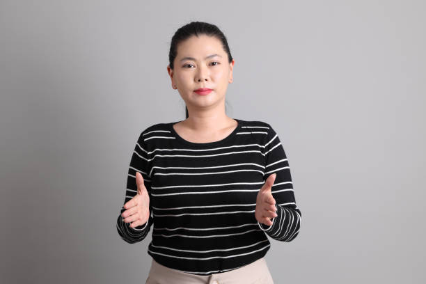 The 40s East Asian woman in the casual clothes with gesture of showing small amount of something or hands showing big and large size sign on the grey background.