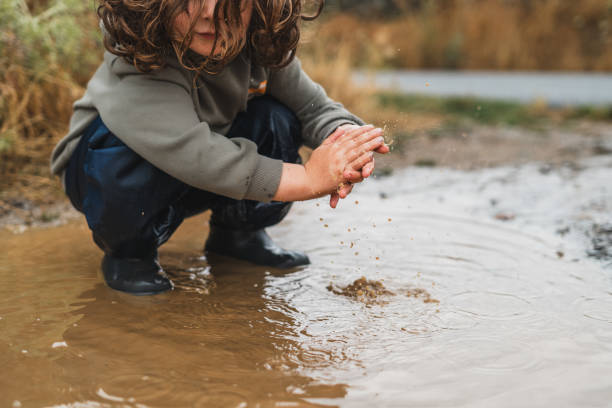 A child is playing in the rain, splashing water and making a mess A child is playing in the rain, splashing water and making a mess. The scene is playful and fun, with the child enjoying the wet and muddy conditions kids dirty shoes stock pictures, royalty-free photos & images