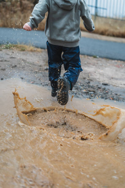 istock A boy is running through a puddle of water, splashing it everywhere 2159898647