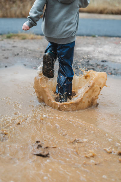 istock A young boy is splashing through a muddy puddle 2159898648