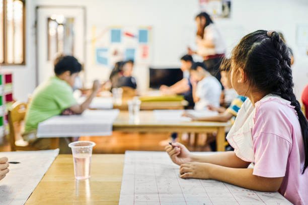 Preteen girl looking away while practicing Chinese calligraphy in a school classroom