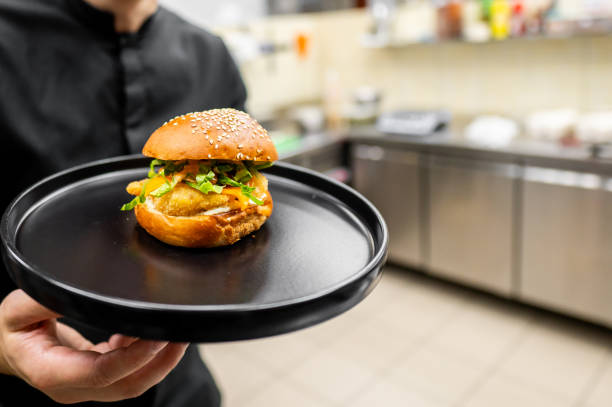 istock A chef holds a burger on a black plate in a kitchen setting 2159899539