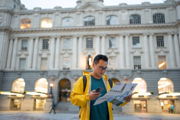 Solo male traveller uses smart phone and city map to find directions